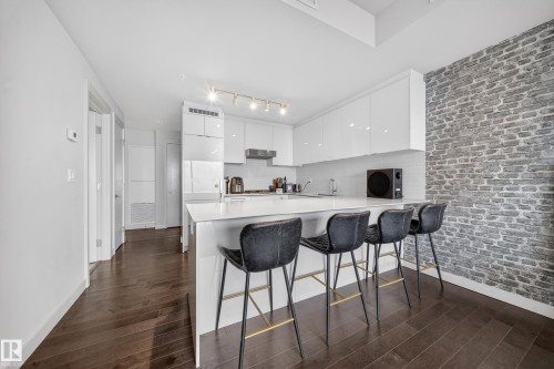 Kitchen featuring a white countertop island, sleek white cabinetry, a subway tile backsplash, and a gray brick accent wall - #4007 10360 102 St Nw, Edmonton, AB 