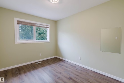Spacious room featuring wood-finish flooring, light green walls, a large window with natural light, and a flush-mount ceiling light fixture - 2439 112 Street Nw, Edmonton, AB - Indoor Photo Showing Other Room