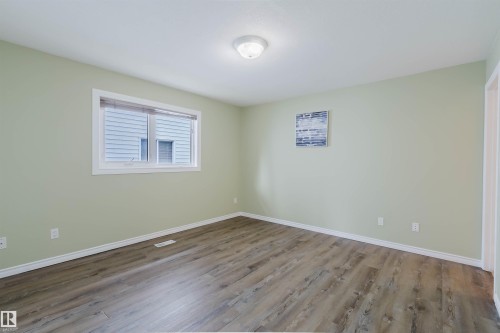 Room featuring wood-finish flooring, light green walls, white trim, and a prominent window with blinds - 2439 112 Street Nw, Edmonton, AB - Indoor Photo Showing Other Room