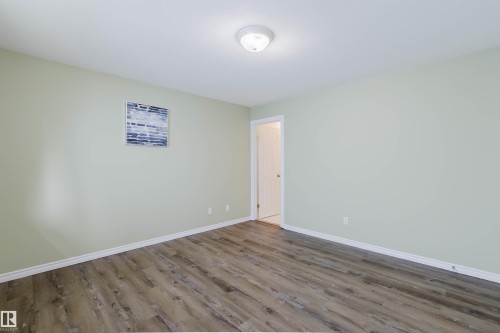 Open room featuring light green walls, wood-finish flooring, white baseboards, and a flush-mount ceiling light - 2439 112 Street Nw, Edmonton, AB - Indoor Photo Showing Other Room