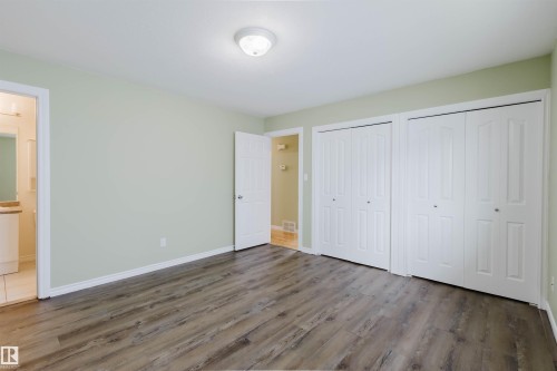 Room featuring wood-finish flooring, two sets of white bi-fold closet doors, and light green painted walls - 2439 112 Street Nw, Edmonton, AB - Indoor Photo Showing Other Room