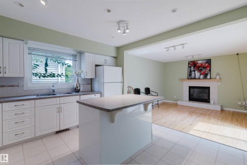 Kitchen featuring white cabinetry, stone-look countertops, and a central island with seating - 2439 112 Street Nw, Edmonton, AB - Indoor Photo Showing Kitchen With Fireplace With Double Sink