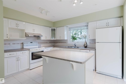 Kitchen featuring white cabinetry, a built-in island, stainless steel range hood, tile flooring, and a large window - 2439 112 Street Nw, Edmonton, AB - Indoor Photo Showing Kitchen With Double Sink