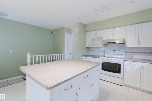 Kitchen featuring a central island with a speckled countertop, white cabinetry with silver hardware, a white range, and a stainless steel range hood - 2439 112 Street Nw, Edmonton, AB - Indoor Photo Showing Kitchen