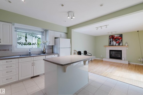 Kitchen featuring white cabinetry, a built-in dishwasher, and a center island with a stone-finish countertop - 2439 112 Street Nw, Edmonton, AB - Indoor Photo Showing Kitchen With Fireplace With Double Sink