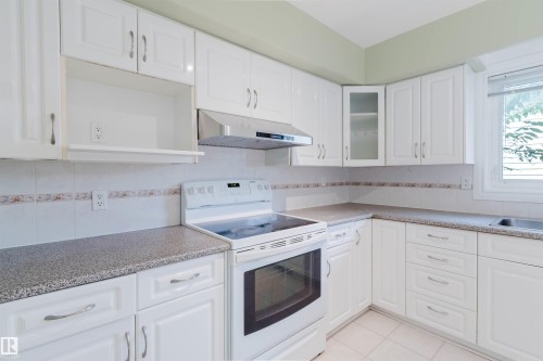 Kitchen featuring white cabinetry, speckled countertops, a tile backsplash with a decorative border, a built-in range hood, and a window with blinds - 2439 112 Street Nw, Edmonton, AB - Indoor Photo Showing Kitchen