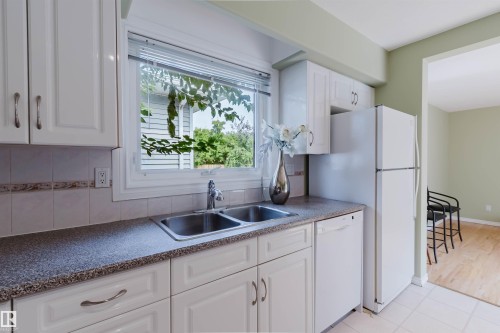 Kitchen featuring white cabinetry, a double basin stainless steel sink with a chrome faucet, speckled laminate countertops, and a full-size white refrigerator - 2439 112 Street Nw, Edmonton, AB - Indoor Photo Showing Kitchen With Double Sink