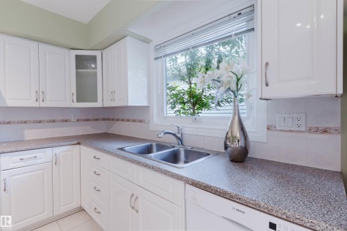 Kitchen featuring white cabinetry, a double basin stainless steel sink, speckled countertops, a tiled backsplash, and a window with natural light - 2439 112 Street Nw, Edmonton, AB - Indoor Photo Showing Kitchen With Double Sink