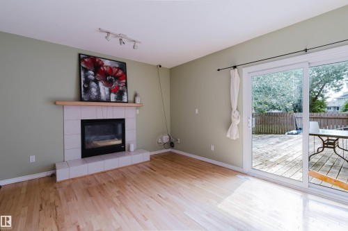 Living area featuring light wood-finish flooring, a tiled fireplace with a wood mantle, and track lighting - 2439 112 Street Nw, Edmonton, AB - Indoor Photo Showing Living Room With Fireplace