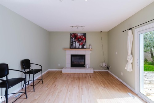 Spacious room featuring wood-finish flooring, a white tiled fireplace with a wood mantel, and light green walls - 2439 112 Street Nw, Edmonton, AB - Indoor Photo Showing Living Room With Fireplace