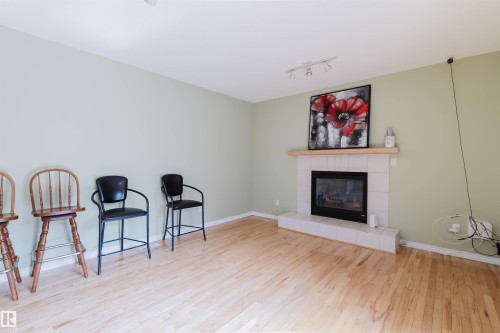 Living area featuring light wood-finish flooring, light green wall paint, and a tiled fireplace with a wood mantle - 2439 112 Street Nw, Edmonton, AB - Indoor Photo Showing Living Room With Fireplace