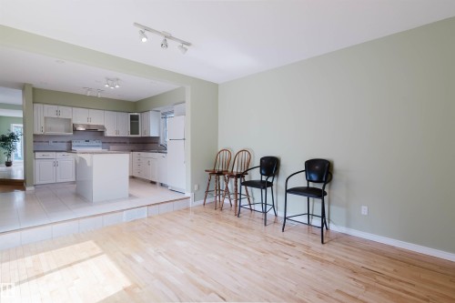 Hardwood-finish flooring leading to a raised kitchen area with white cabinetry, a central island, and tile flooring - 2439 112 Street Nw, Edmonton, AB - Indoor Photo Showing Kitchen