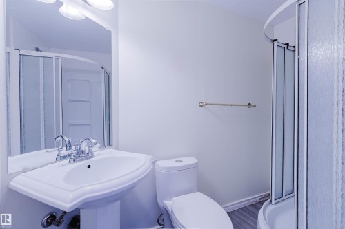 Contemporary bathroom featuring a pedestal sink, chrome fixtures, a toilet, a curved shower enclosure with frosted glass, and wood-finish flooring - 2439 112 Street Nw, Edmonton, AB - Indoor Photo Showing Bathroom