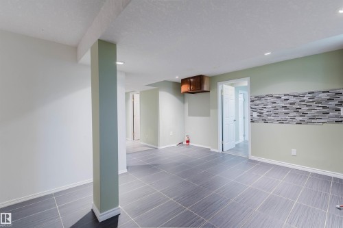 Spacious finished interior with large format floor tiles, recessed lighting, accent wall with mosaic tile, and a built-in wood-finish cabinet - 2439 112 Street Nw, Edmonton, AB - Indoor Photo Showing Other Room