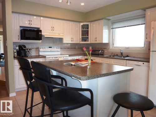 Kitchen featuring a central island with a speckled countertop, white cabinetry, integrated sink, and an overhead microwave - 2439 112 Street Nw, Edmonton, AB - Indoor Photo Showing Kitchen With Double Sink