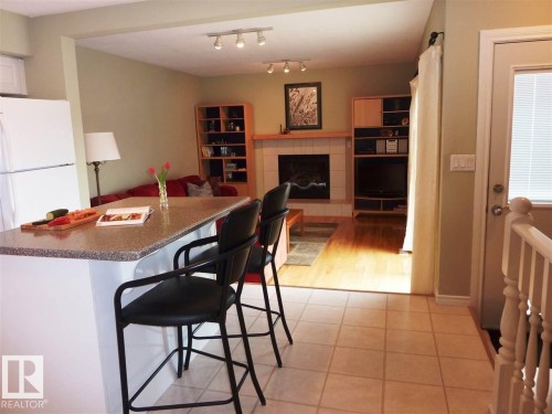 Kitchen island with a speckled countertop and integrated seating, contrasting with the light-toned tile flooring - 2439 112 Street Nw, Edmonton, AB - Indoor Photo Showing Other Room With Fireplace