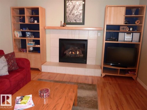 Central fireplace featuring a tile surround and hearth, flanked by built-in shelving units - 2439 112 Street Nw, Edmonton, AB - Indoor Photo Showing Living Room With Fireplace