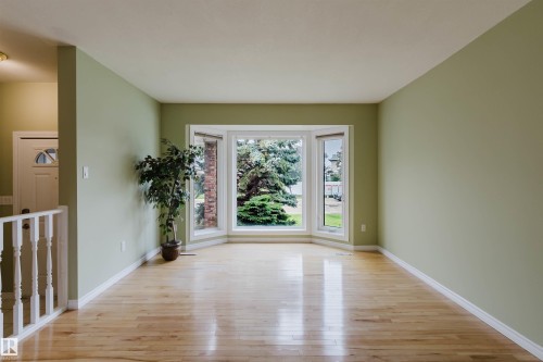 Spacious room featuring light wood-finish flooring, light green walls, white baseboards, and a prominent bay window - 2439 112 Street Nw, Edmonton, AB - Indoor Photo Showing Other Room