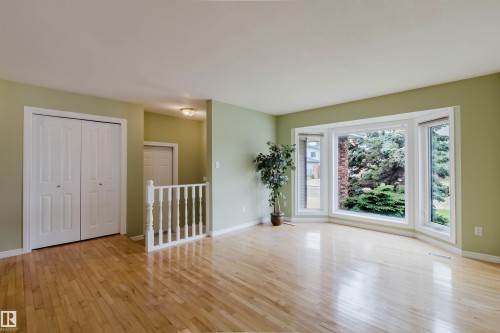 Bay window offering exterior views, wood-finish flooring, light green wall paint, white baseboards, and bi-fold closet doors - 2439 112 Street Nw, Edmonton, AB - Indoor