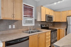 Kitchen featuring wood cabinetry, stainless steel appliances, a double basin sink, and a tile backsplash - 