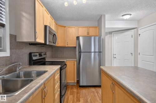 Kitchen featuring light wood cabinetry, stainless steel appliances, a double basin sink, neutral countertops, and wood-finish flooring - 21312 48 Avenue Nw, Edmonton, AB 