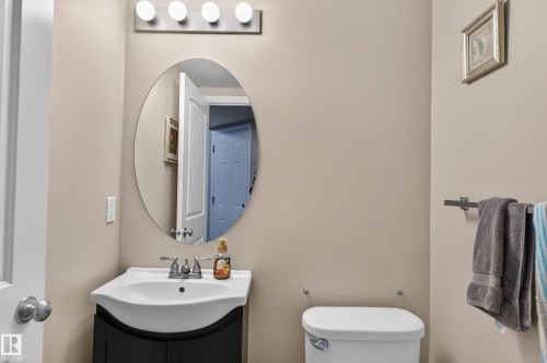 Bathroom featuring an oval mirror, a vanity with a white basin and dark cabinetry, and a four-bulb vanity light fixture - 21312 48 Avenue Nw, Edmonton, AB 