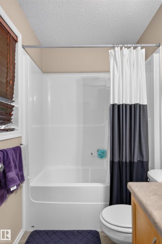 Shower-over-tub combination with white surround, brown wood-finish blinds, and a built-in toilet - 21312 48 Avenue Nw, Edmonton, AB 