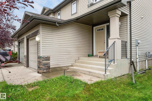 Beige siding exterior with stone accent columns, two-car garage, and concrete steps with a black metal handrail - 21312 48 Avenue Nw, Edmonton, AB 