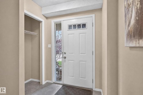 Welcoming foyer featuring a six-panel white entry door with decorative glass panels, neutral-toned walls, recessed ceiling detail, ceramic tile flooring, and a spacious coat closet with wire shelving - 21312 48 Avenue Nw, Edmonton, AB 