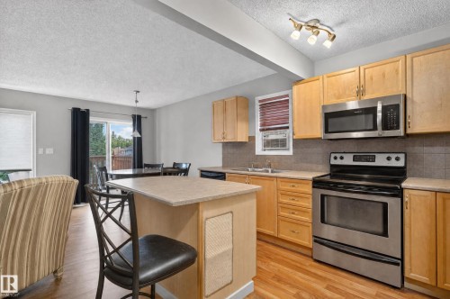 Kitchen featuring wood-finish flooring, light wood cabinetry, stainless steel appliances, and a peninsula island with an integrated breakfast bar - 21312 48 Avenue Nw, Edmonton, AB 