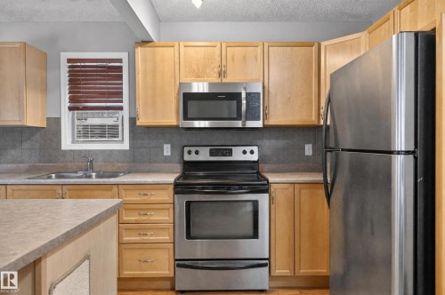 Kitchen featuring stainless steel appliances, light wood-finish cabinetry, a large basin sink, and tile backsplash - 21312 48 Avenue Nw, Edmonton, AB 