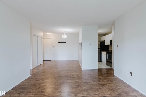 Wood-finish flooring, white walls, built-in closet with sliding doors, ceiling-mounted lighting fixtures, and an open doorway to the kitchen area - #316 17109 67 Av Nw, Edmonton, AB 