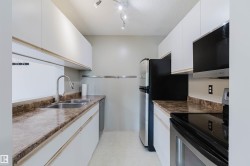 Galley kitchen featuring white cabinetry, brown patterned countertops, stainless steel appliances, a dual basin sink, and a built-in microwave - 
