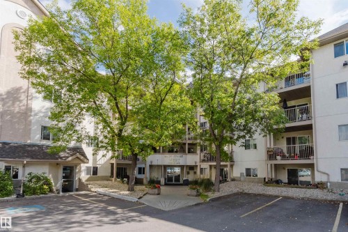 Multi-story building featuring balconies, mature trees, and a paved parking area - #316 17109 67 Av Nw, Edmonton, AB 
