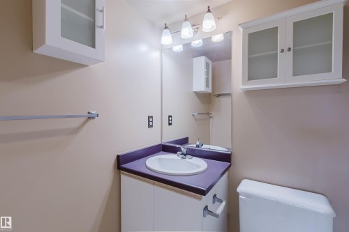 White vanity with an integrated sink, complemented by a large mirror and wall-mounted lighting - #316 17109 67 Av Nw, Edmonton, AB 