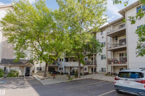 Multi-story building with white exterior, multiple private balconies, and a paved parking area - #316 17109 67 Av Nw, Edmonton, AB 