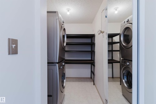 Laundry area with stacked washing machine and dryer, overhead lighting, and built-in shelving - #316 17109 67 Av Nw, Edmonton, AB 