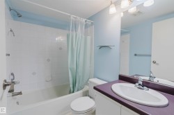 Vanity with integrated sink and chrome faucet, large wall mirror, built-in bathtub with shower, white tile surround with decorative inlays, and overhead lighting fixture - 