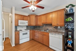 Kitchen featuring wood-finish flooring, wood cabinetry, built-in microwave, dual basin stainless steel sink, and a ceiling fan - 