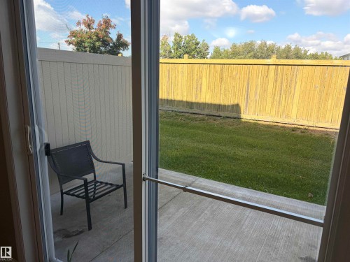 Sliding glass patio door with a screen, opening to a concrete patio and a fenced backyard with a manicured lawn - #100 13825 155 Av Nw, Edmonton, AB 