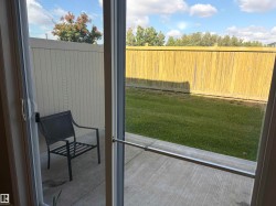 Sliding glass patio door with a screen, opening to a concrete patio and a fenced backyard with a manicured lawn - 