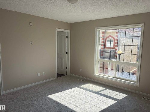 Neutral tone wall paint, light gray carpeting, white trim, and a window with grid inserts - #100 13825 155 Av Nw, Edmonton, AB 