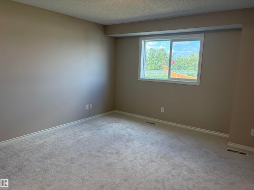 Carpeted interior space with a neutral wall finish, white trim, and a prominent window - #100 13825 155 Av Nw, Edmonton, AB 