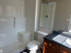 White shower/tub combination with built-in shelving, white toilet, single vanity with wood cabinetry, dark countertop, and integrated sink - 