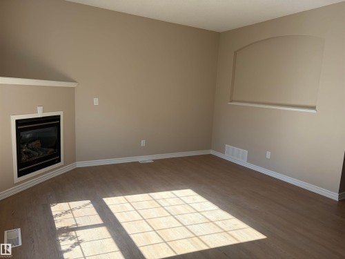 Corner fireplace with black insert, wood-finish flooring, and a decorative wall niche with an arched top - #100 13825 155 Av Nw, Edmonton, AB 