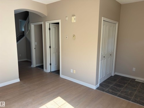 Wood-finish flooring, neutral wall paint, white trim, dark tile flooring, and a bifold closet door - #100 13825 155 Av Nw, Edmonton, AB 