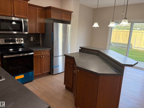 Kitchen featuring wood-finish cabinetry, stainless steel appliances, a tiered island, and pendant lighting - #100 13825 155 Av Nw, Edmonton, AB 