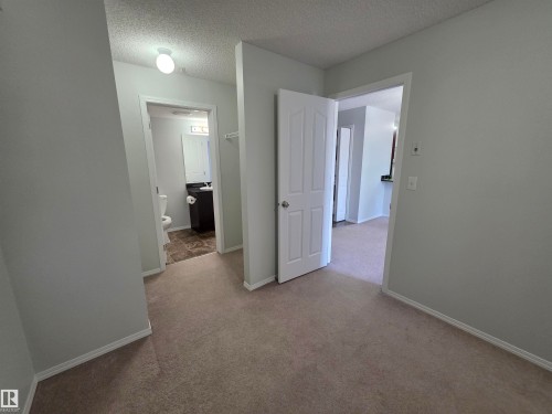 Plush carpeting throughout the main area, leading to a bathroom featuring tile flooring, a built-in vanity, and a toilet - #206 12045 22 Av Sw, Edmonton, AB 