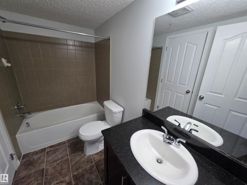 Dual vanity bathroom featuring white ceramic sinks, black countertop with integrated backsplash, chrome faucetry, and tile flooring - #206 12045 22 Av Sw, Edmonton, AB 