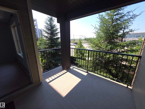 Covered balcony featuring a textured floor, black metal railing, and an adjacent sliding glass door - #206 12045 22 Av Sw, Edmonton, AB 